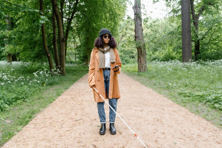 Femme élégante en manteau explore un parc verdoyant avec une canne, utilisant son smartphone pour se guider